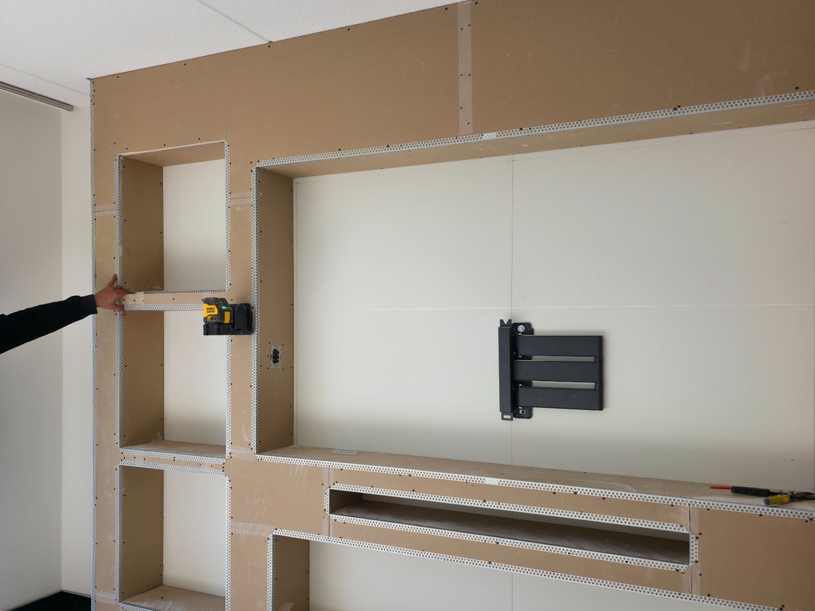 Cinewall bouwen: frame met gipsplaten en uitgespaarde nissen voor tv, haard en verlichting, met de tv-beugel al op de wand gemonteerd