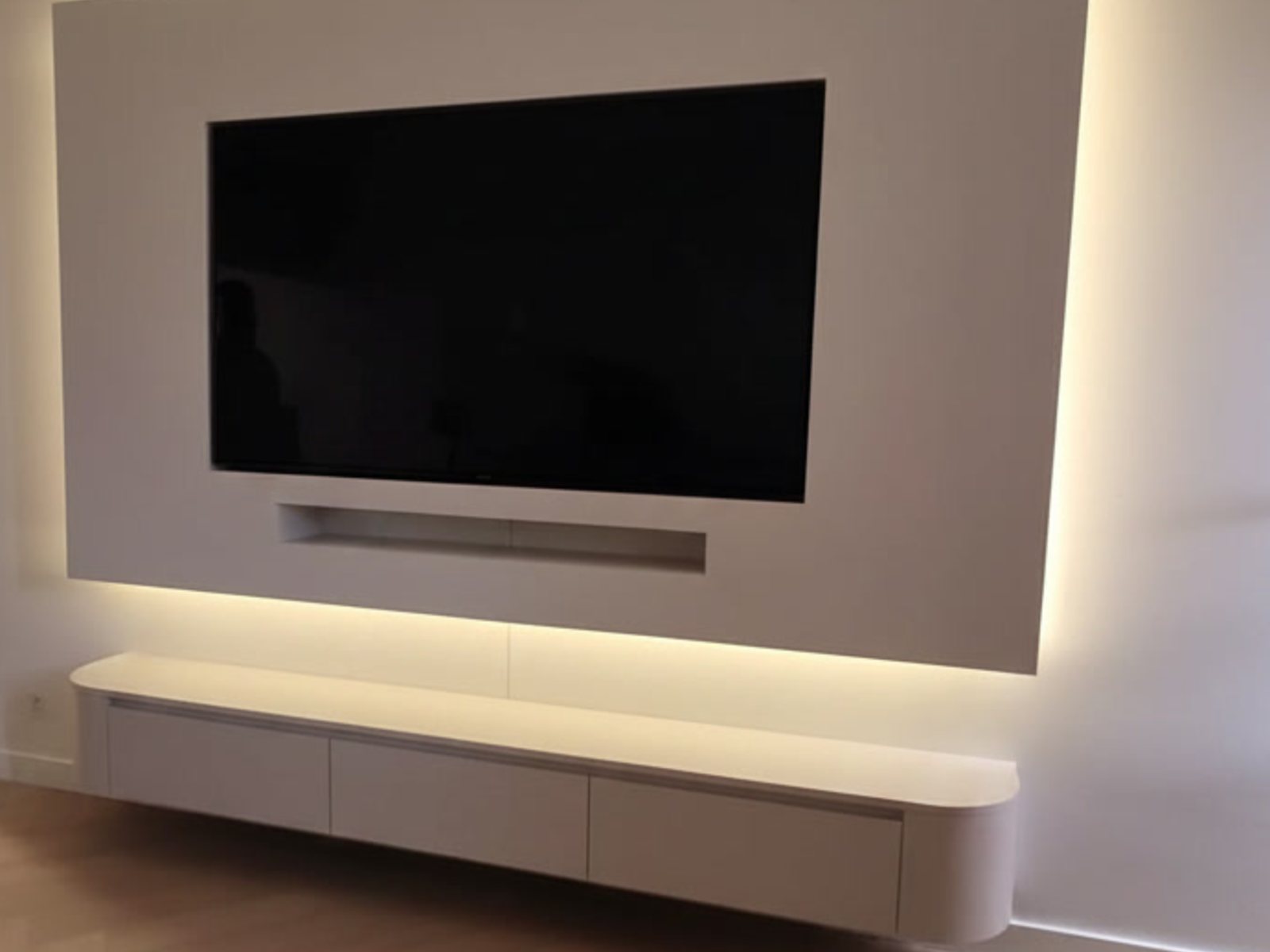 Cinewall met vakken en kasten: greeploze lades in een afgerond zwevend meubel onder een verlicht wandpaneel